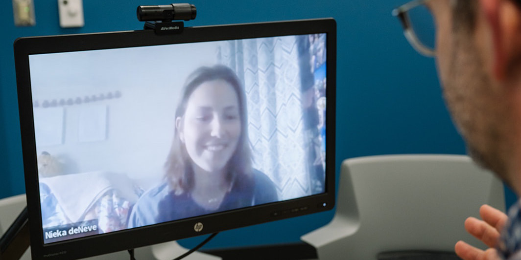 Two people on a Zoom call. One on the screen virtually and one in person.